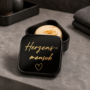 Schwarze personalisierte Aufbewahrungsdose für Shampoo-Bars mit goldener Aufschrift „Herzensmensch“, gefüllt mit einem handgemachten Naturleise Shampoo-Bar mit Kamille und Ringelblume.